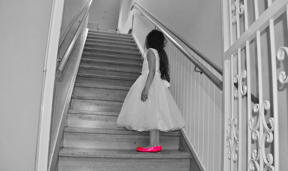 Black & White Photo Of A Girl With Pink Shoes Walking Up A Staircase.